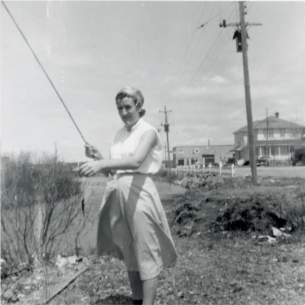 g — 1956 — pêche — Tags: pêche, rivière — Gisèle Bouchard à la pêche, derrière : épicerie et garage